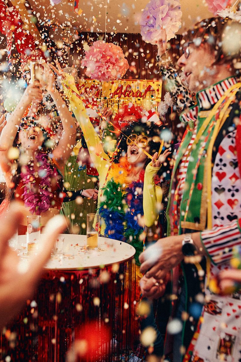 People in costumes are dancing and singing in a room covered with confetti.