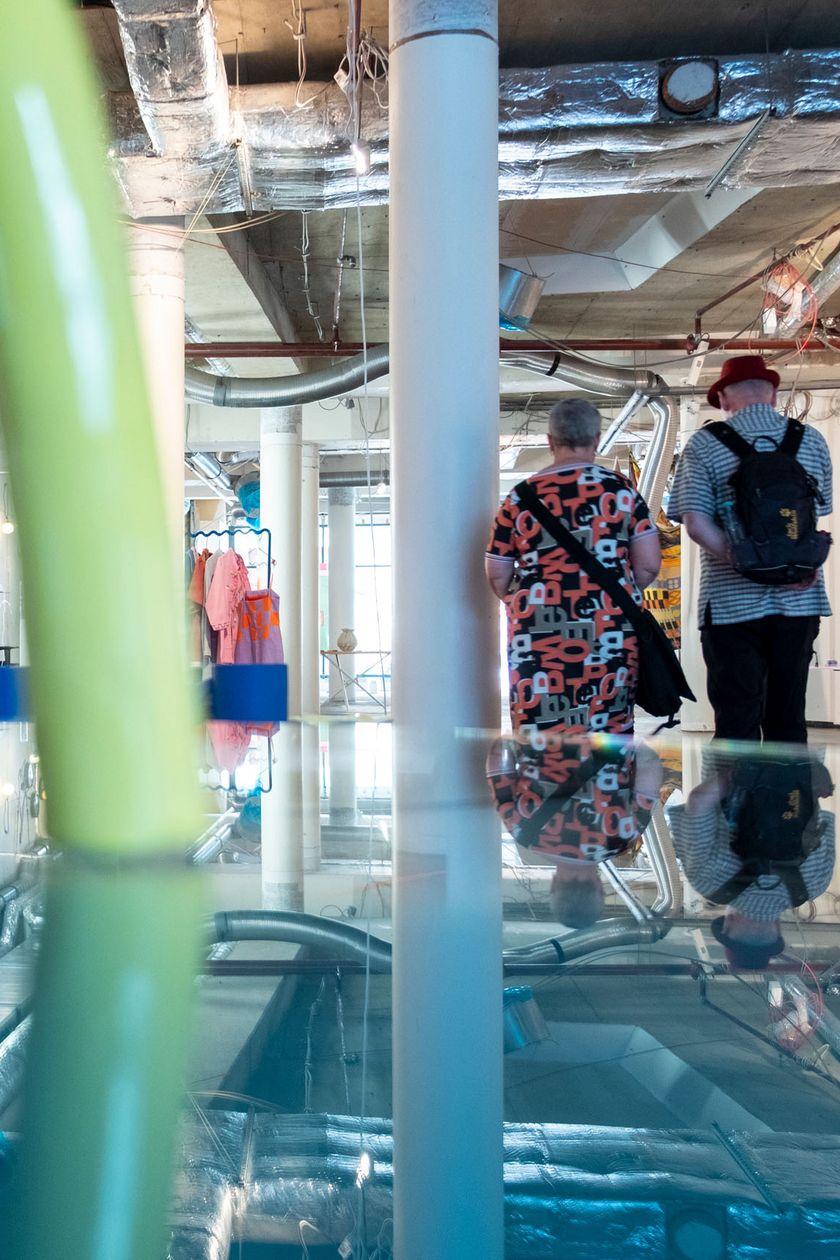 In a bright industrial space, colorful artworks and objects are scattered around.
