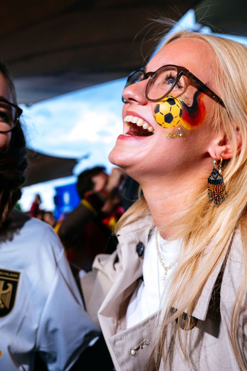 Two women in jerseys are cheerful and laughing. Flags decorate their cheeks.