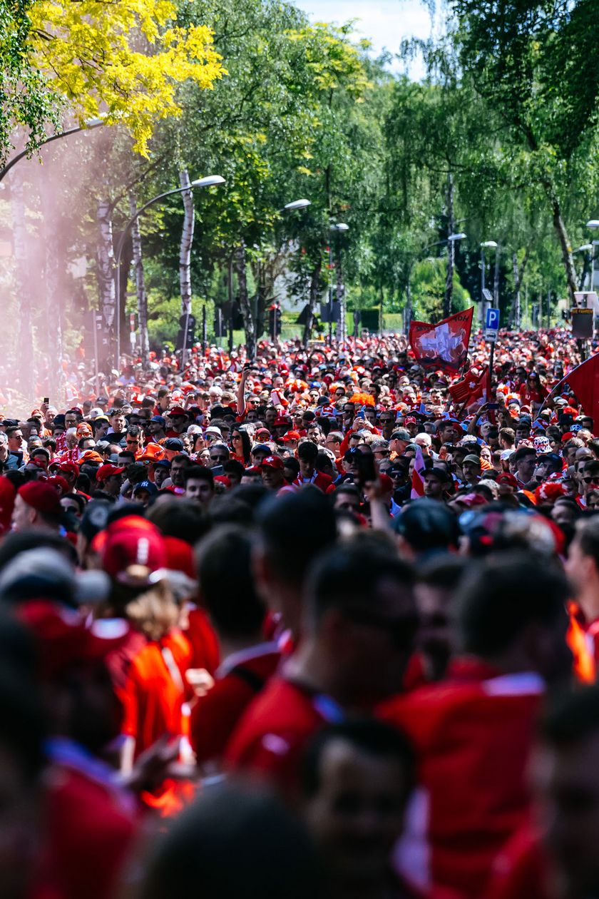 Hundreds of people in red jerseys are running through an avenue in the sunshine. The atmosphere seems peaceful.