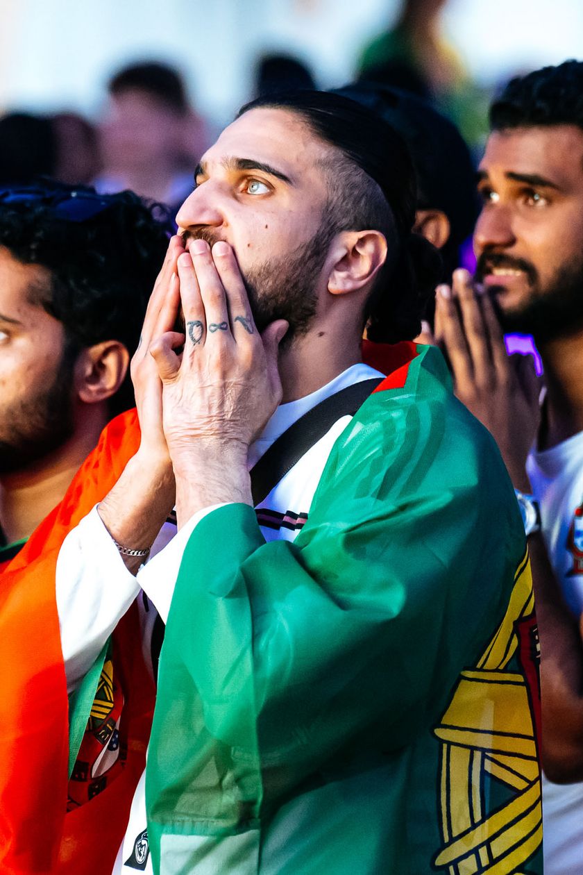 Three fans with flags draped over their shoulders look nervously upwards.