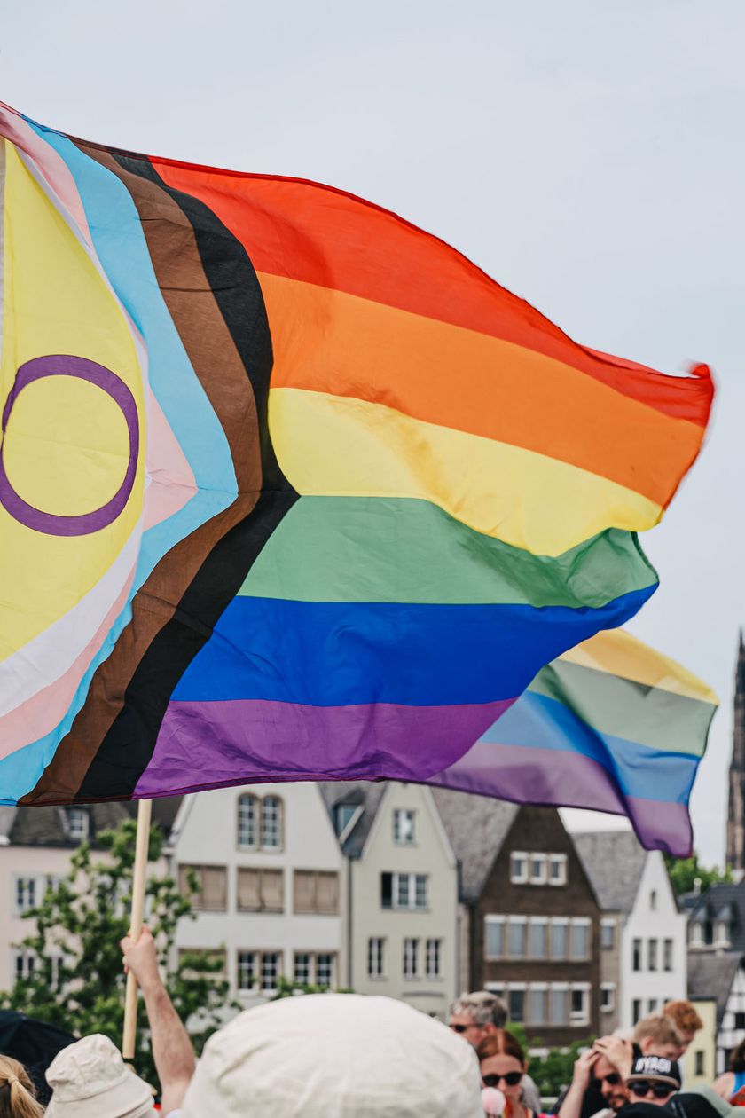 A colorful flag flutters in the wind. In the background, you can see the old town of Cologne and the cathedral.