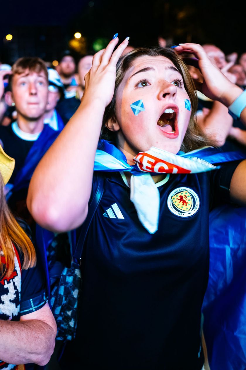 A young woman with flags on her cheeks holds both arms to her head in dismay. An older lady with a yellow hat looks disappointedly into the distance.