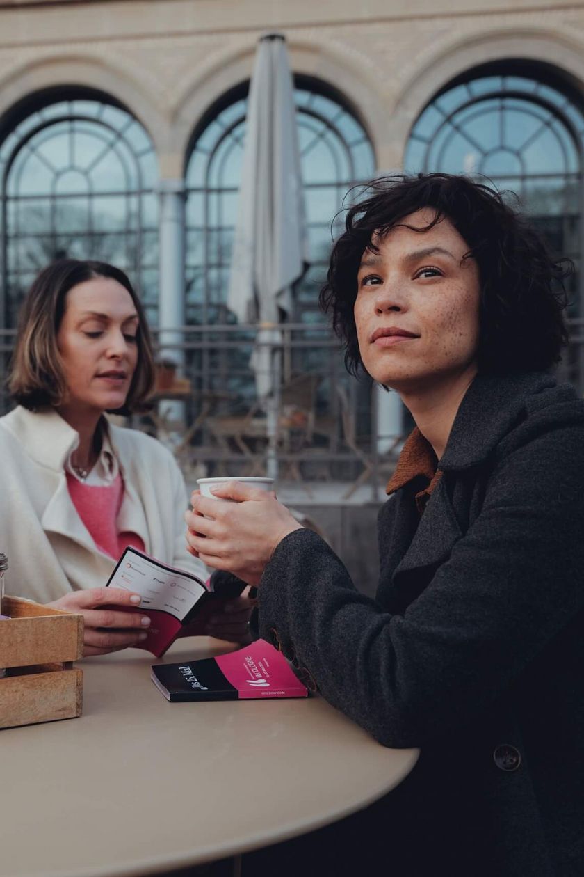 Two people are standing at a table in front of the building in the Flora.