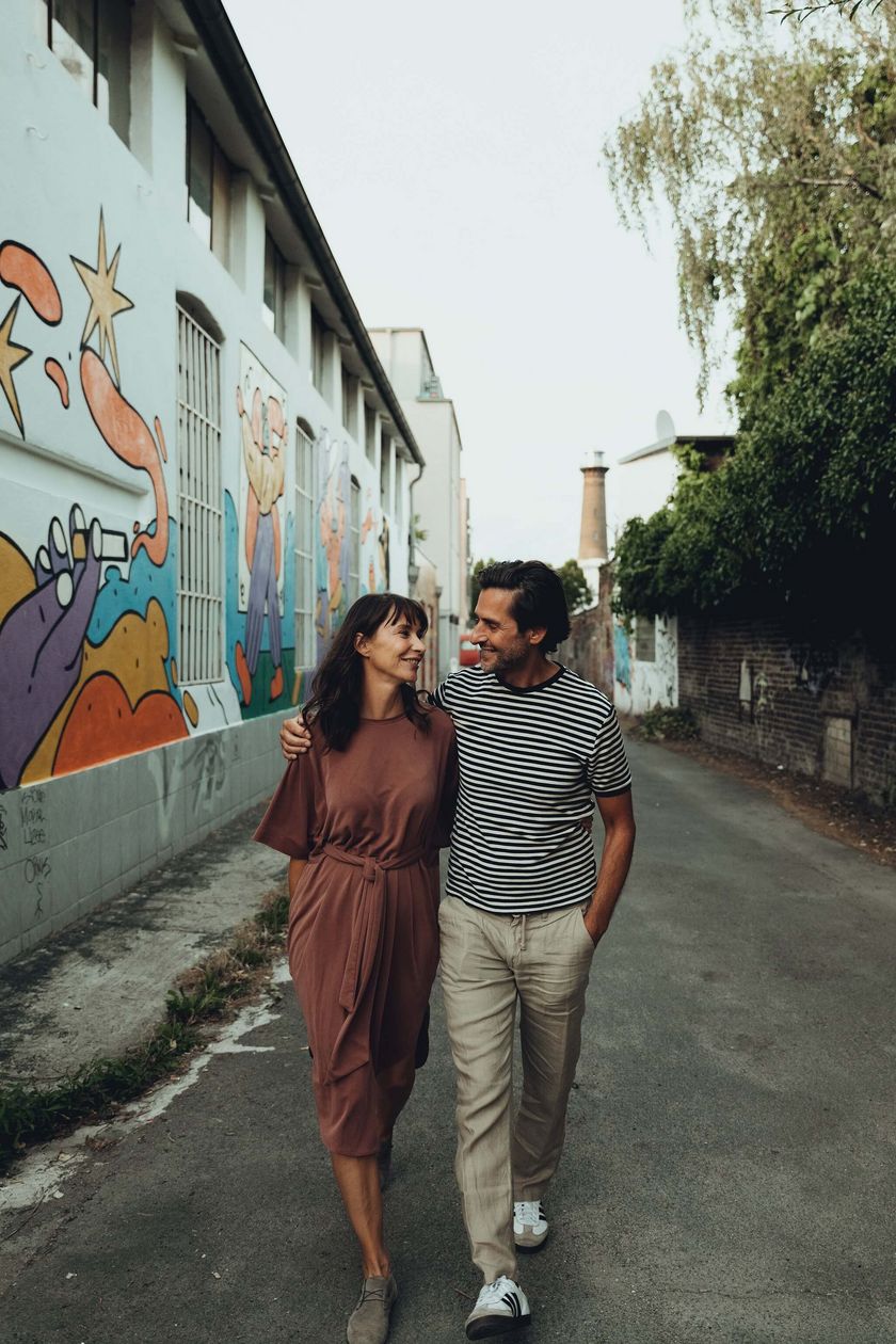Two people walk along a street, their arms draped over each other's shoulders.
