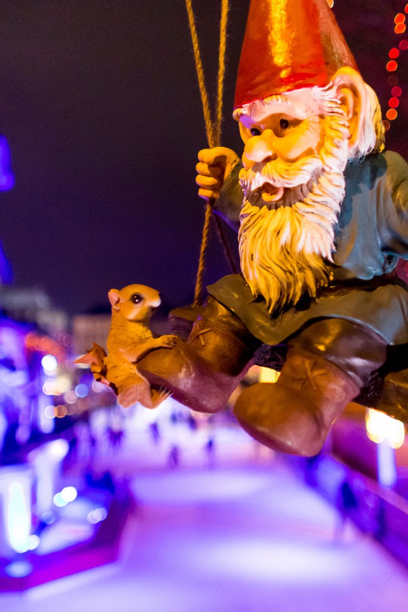 A festively illuminated Christmas market with colorful lighting, a swinging Heinzelmann in close-up.