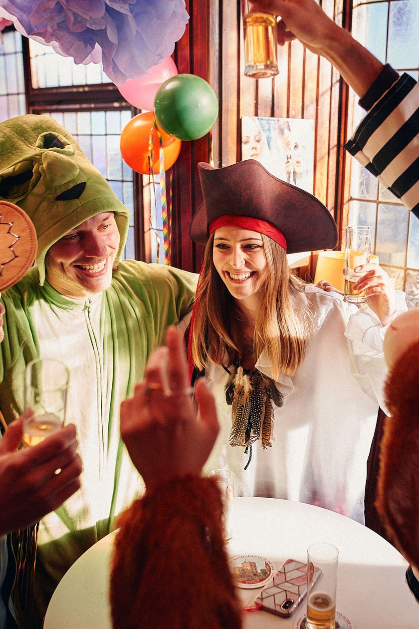 Five colorfully dressed people stand around a round standing table. They sway and appear cheerful.