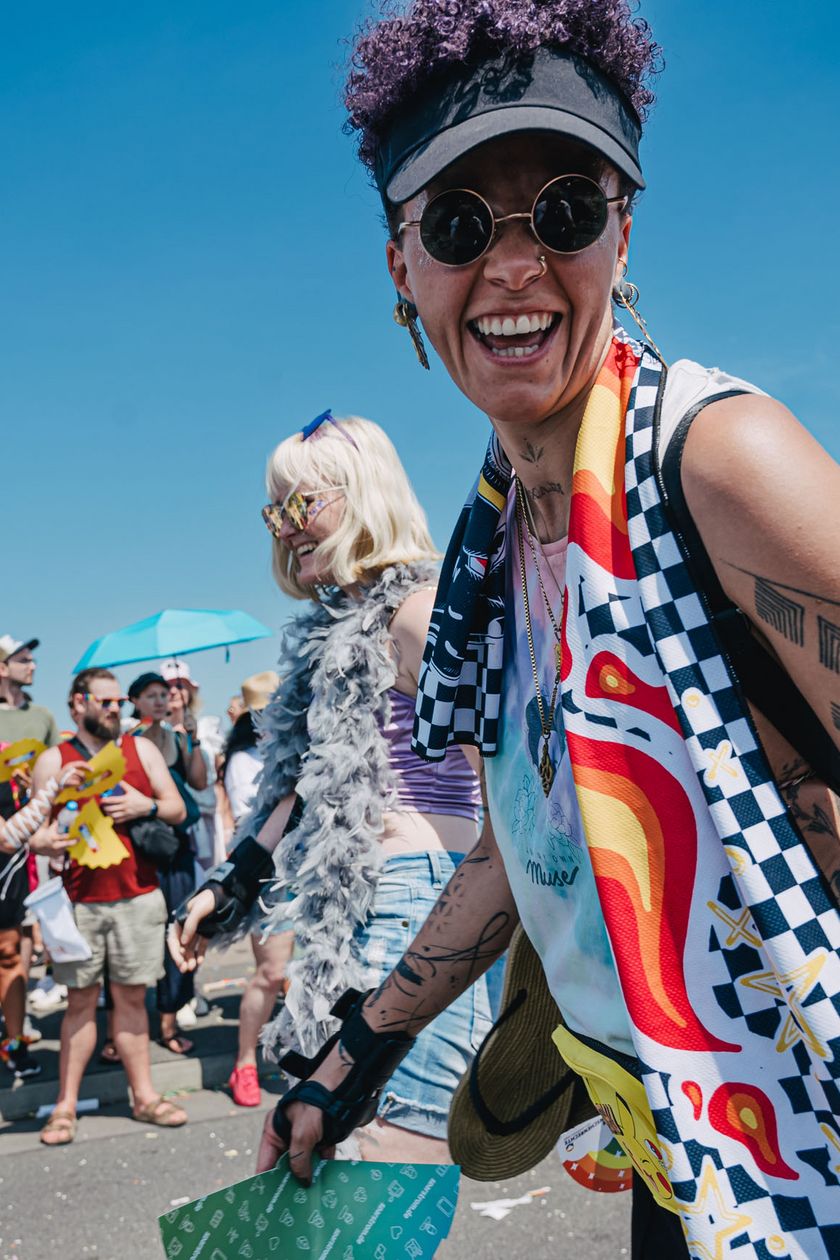 Two people are joyfully participating in the Pride demonstration. People are standing by the roadside.