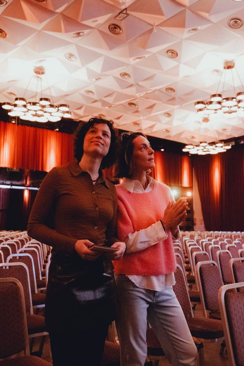 Two people stand in a warmly lit hall and look around.