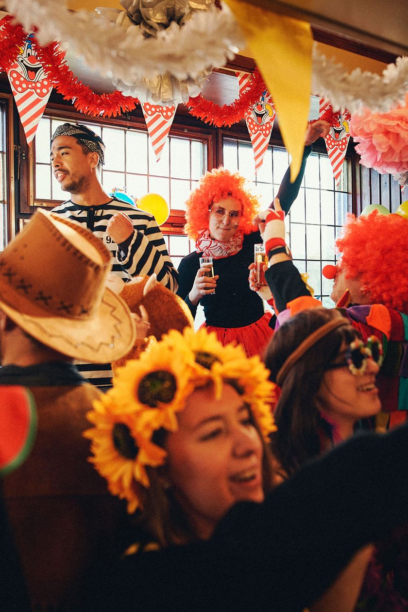 A colorfully decorated pub with paper garlands, pennants, and streamers. A group of costumed people dancing and singing.
