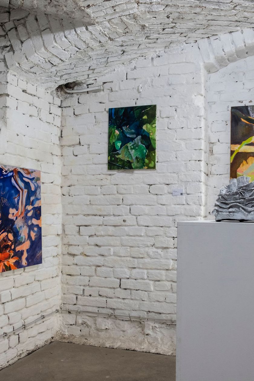 A vaulted cellar with white-painted brick walls. Colorful abstract paintings hang on the walls.