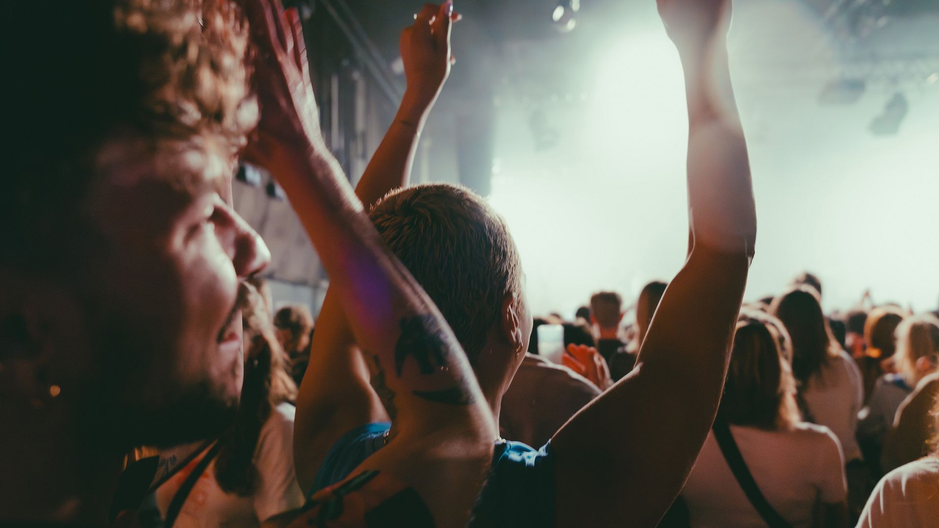 A person raises their arms at a concert. Around them, a crowd of people.
