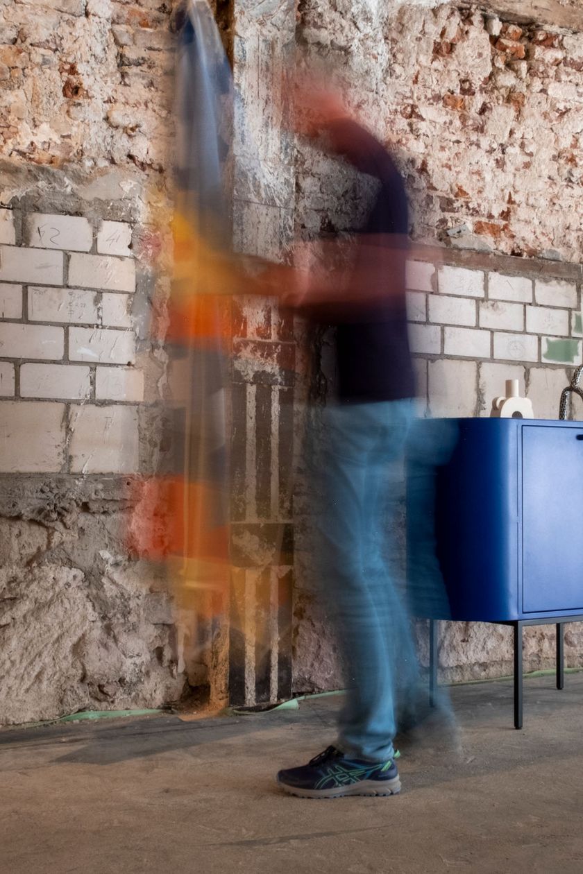 In front of an untreated brick wall stand blue designer furniture pieces.