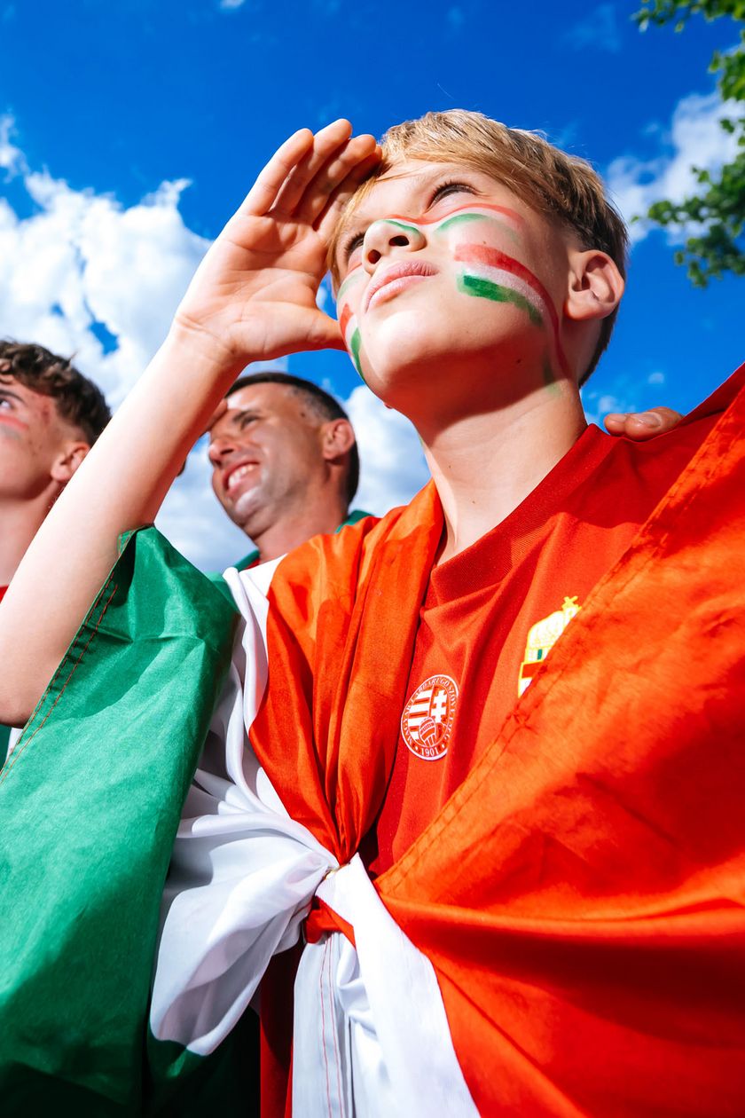 Three fans with flags draped over their shoulders stare eagerly ahead. Flags adorn their cheeks.
